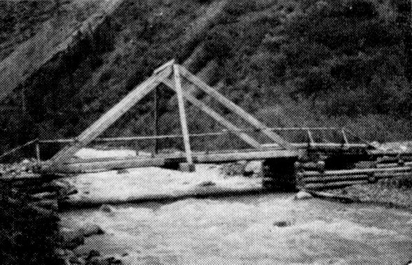 A simple wooden truss bridge crossing a stream of about twenty feet