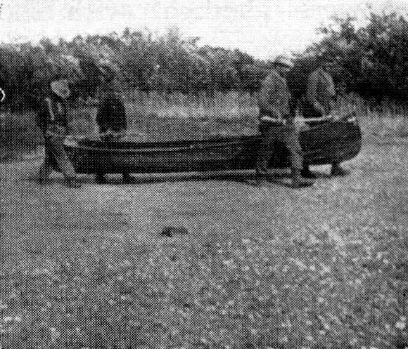 Four men carrying a canoe through a wetland